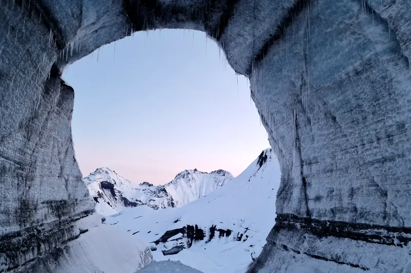 Arco de hielo dentro de una cueva glaciar con vista a la montaña nevada
