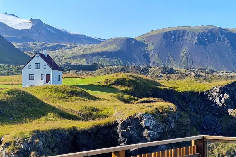 Casa blanca entre colinas verdes y rocas de lava frente a las montañas de Arnarstapi