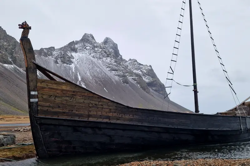 Réplica de barco vikingo varada en la orilla bajo montañas nevadas en Stokksnes