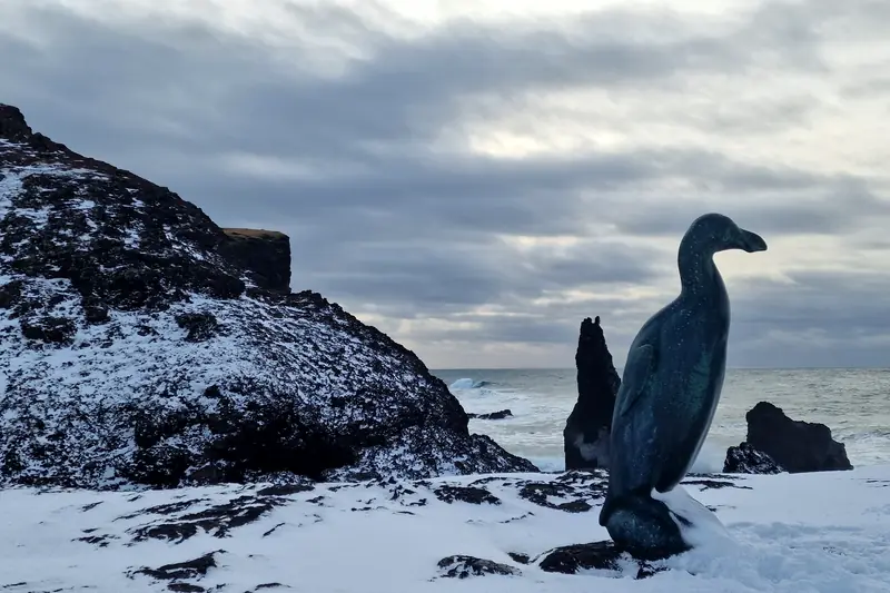 Escultura de un gran alca frente al mar en la costa nevada de Reykjanes