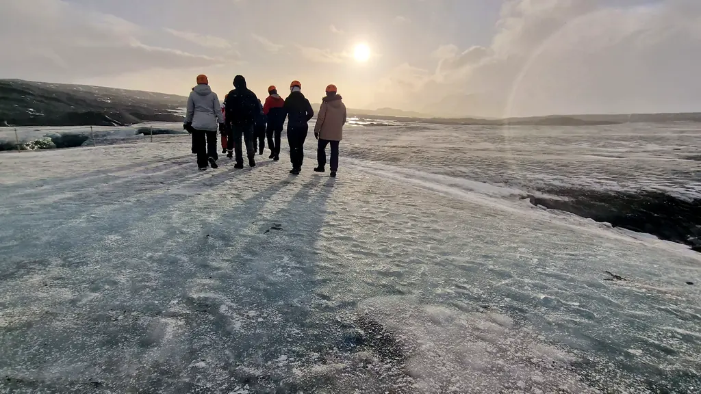 Grupo de viajeros con casco caminando sobre un glaciar de Islandia a contraluz