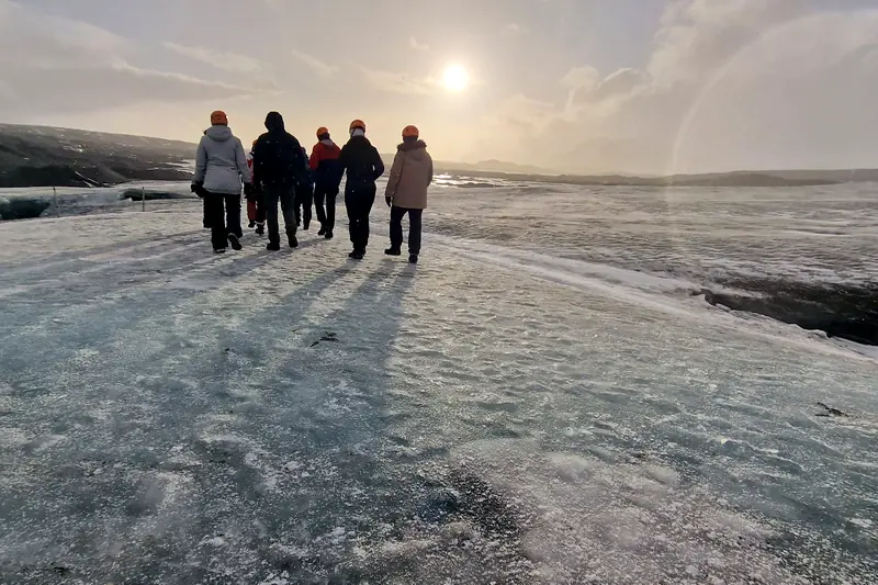Grupo de viajeros con cascos caminando sobre el hielo de un glaciar a contraluz