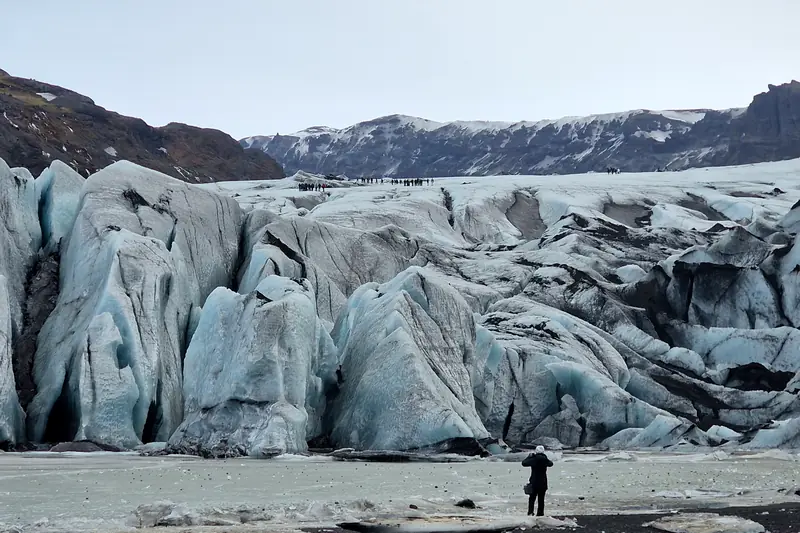 Viajero frente a la lengua de un glaciar con hielo azul y gris